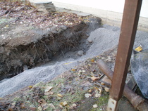 Soralla peitetty viemäri ja kaivanto lähellä talon seinää. Kuvan oikeassa alareunassa osa vanhaa viemäriputkea ja kaivon kansi.